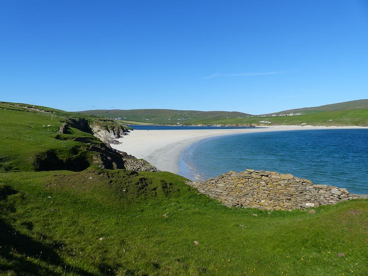 Looking back from St Ninian's Isle across the white sand causeway to Shetland's Mainland, a drystone ruin on the green slope below.
