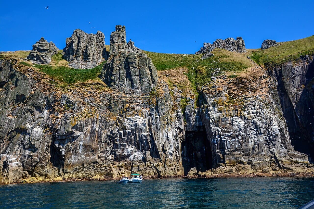 Granite pinnacles and seabird-stained cliffs tower over a small boat at Jenny's Cove on Lundy's west coast.