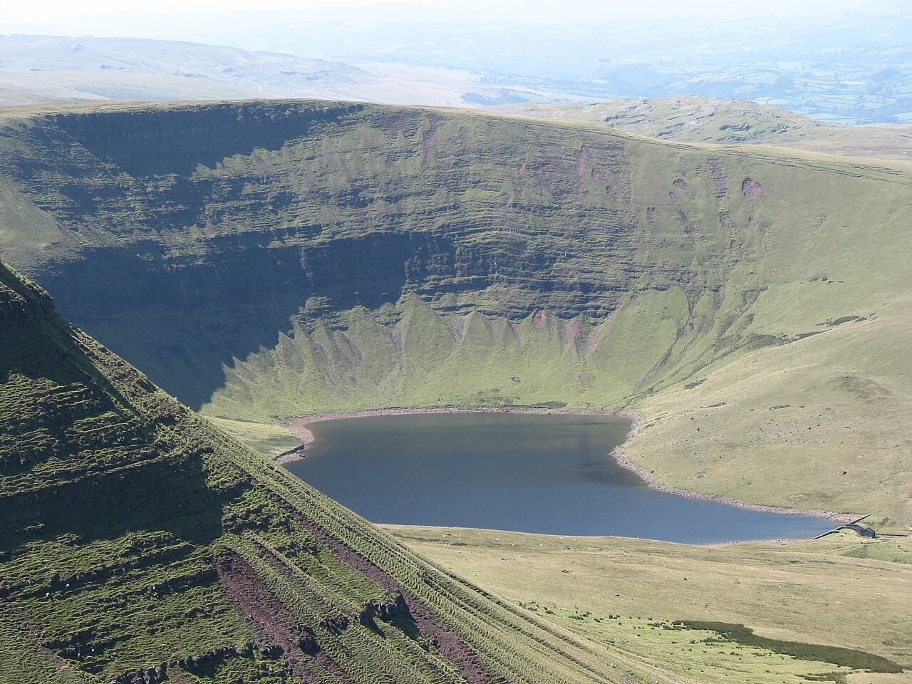 Llyn y Fan Fach lies dark and still in its glacial cwm below the green escarpment of Bannau Sir Gaer.