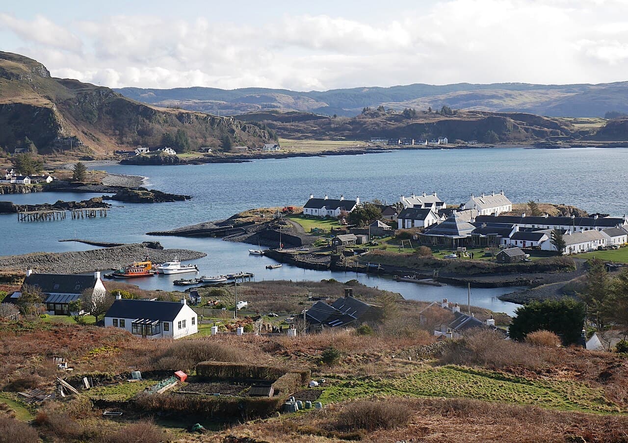 White cottages, flooded quarry pools and the small harbour of Easdale seen from above, with Easdale Sound and the hills of Seil beyond.
