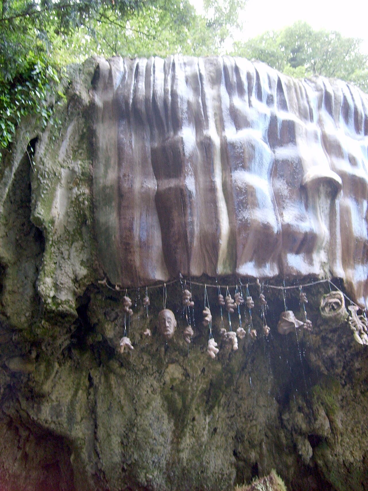 The bulging flowstone dome of the Petrifying Well at Knaresborough, ribbed like a waterfall frozen mid-fall, with offerings strung beneath it.