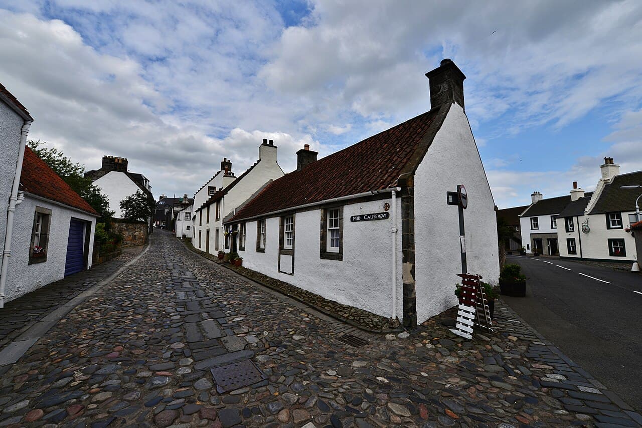An empty cobbled lane forks and climbs around white-harled cottages with red pantile roofs at Mid Causeway in Culross.