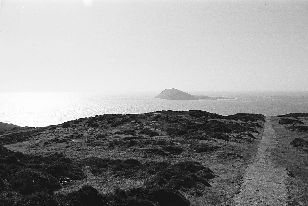 Bardsey Island rises like a whale across the glittering waters of Bardsey Sound, seen from a path at the tip of the Llŷn Peninsula.