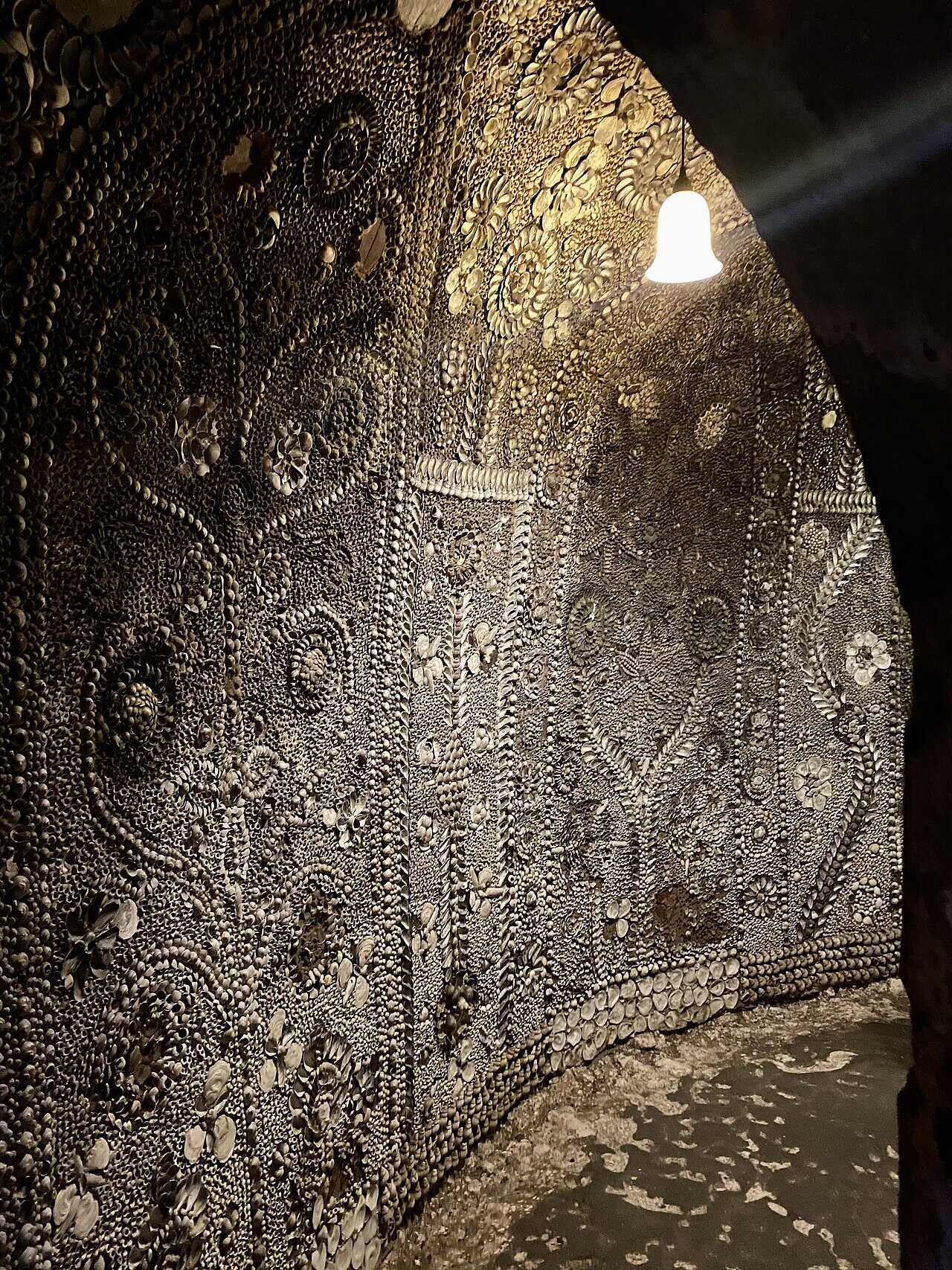 A curving passage lined floor to ceiling with panels of shell mosaic, glowing under a single bell-shaped lamp.