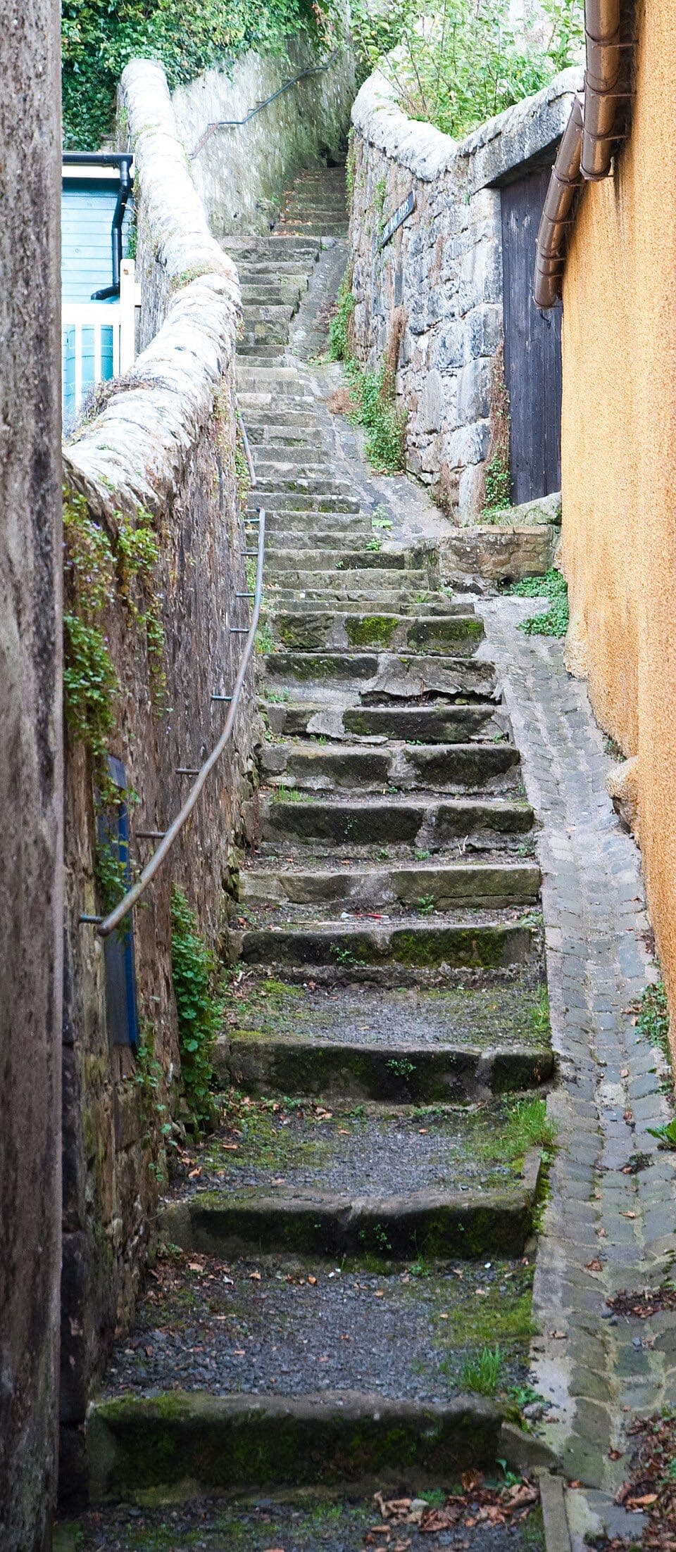 Moss-edged stone steps climb a narrow close between lichened rubble walls and the warm ochre gable of a cottage in Culross.