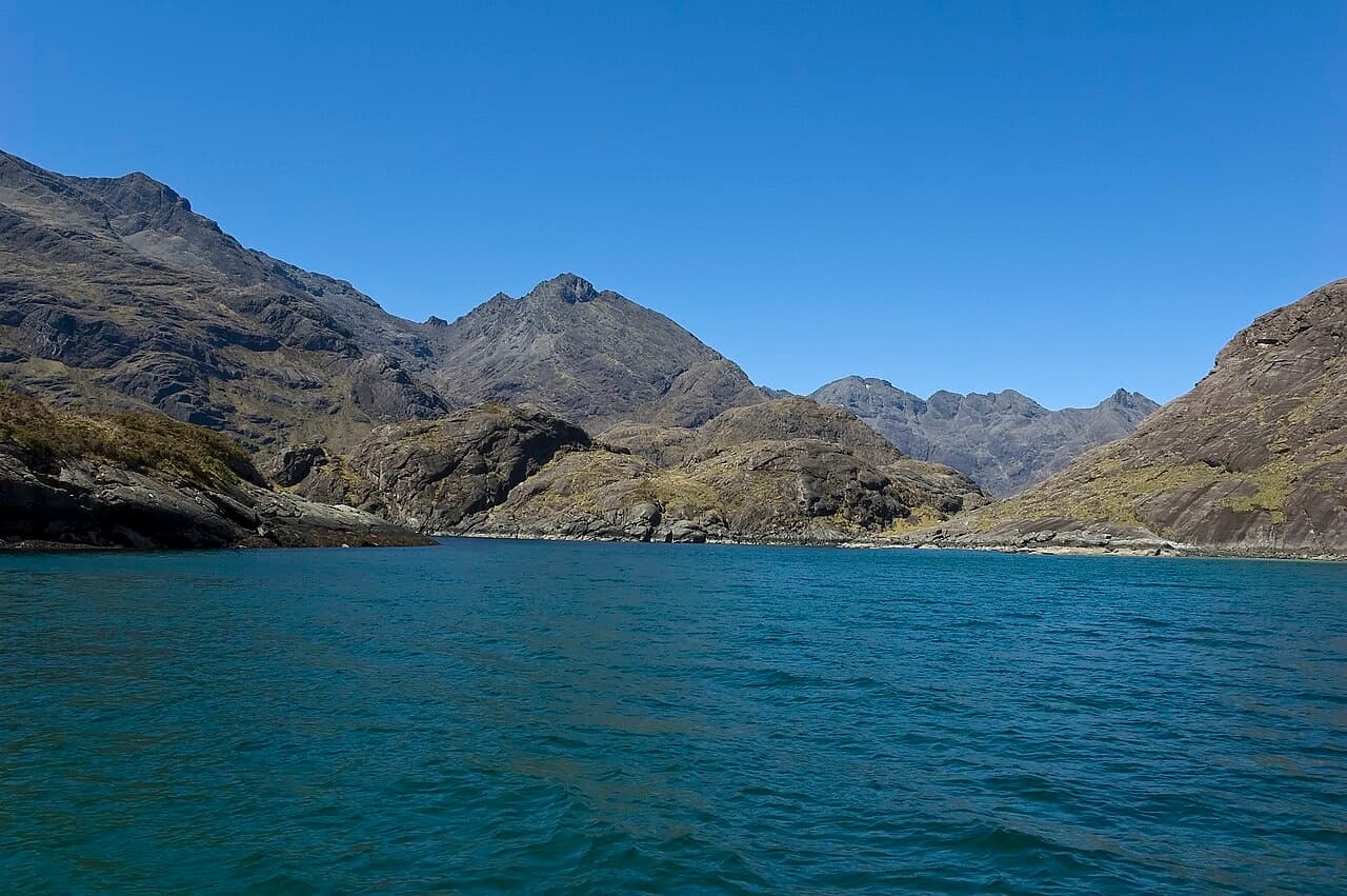 Calm blue water of Loch na Cuilce, the sea-loch landing place for Loch Coruisk, with the Black Cuillin ridge rising beyond the shore.