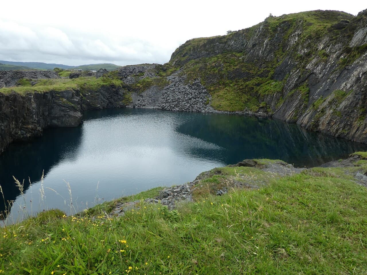 Dark water fills a deep abandoned slate quarry on Easdale, enclosed by sheer rock walls fringed with rough grass.