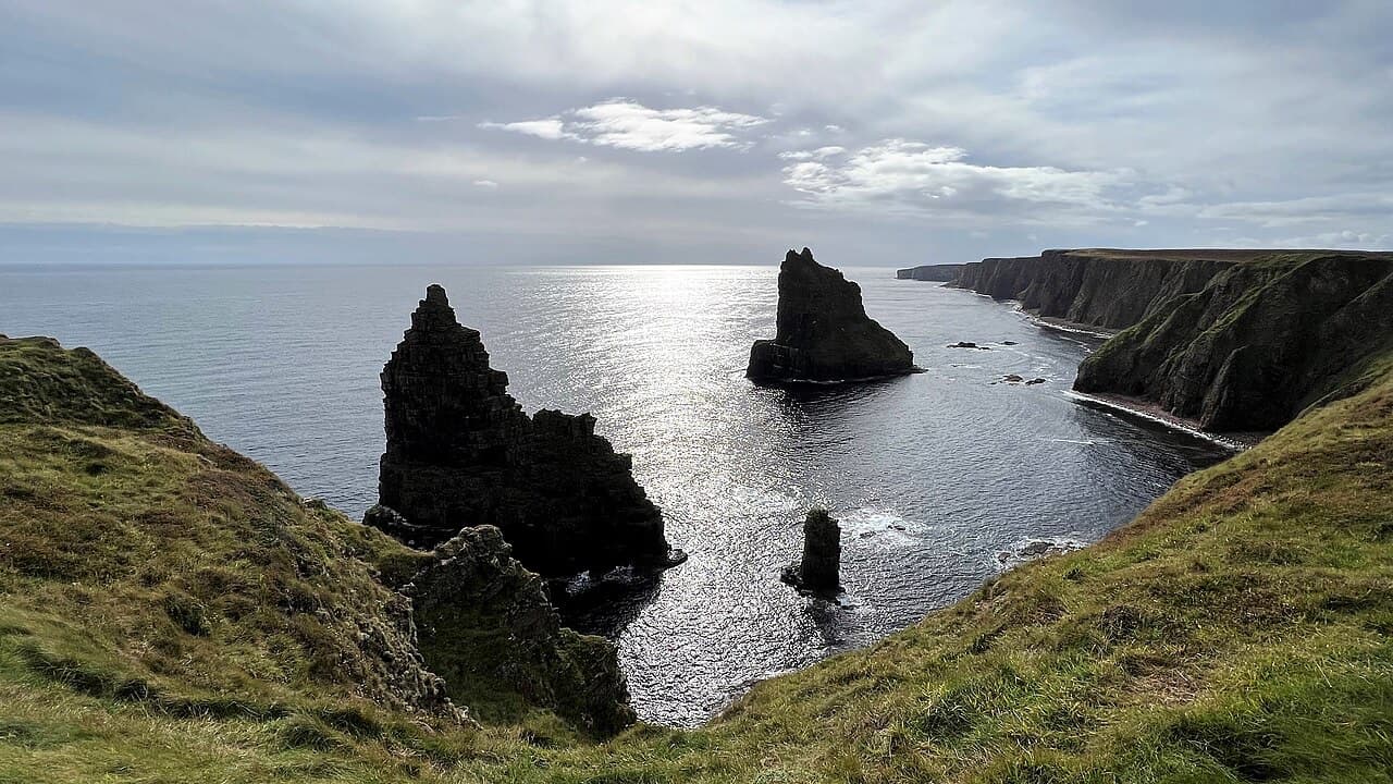 Low silver light on the sea behind the dark Stacks of Duncansby, the cliffs receding south along the coast.